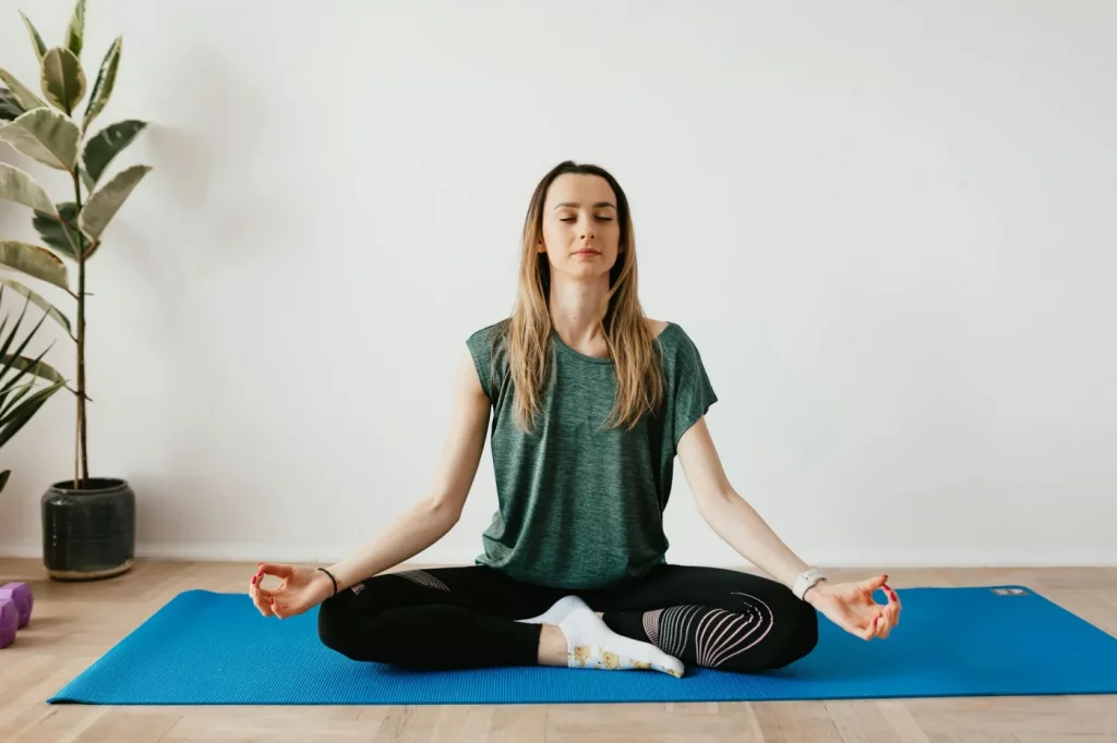 Woman practicing 4-7-8 breathing technique in a calm home yoga space with plants and closed eyes