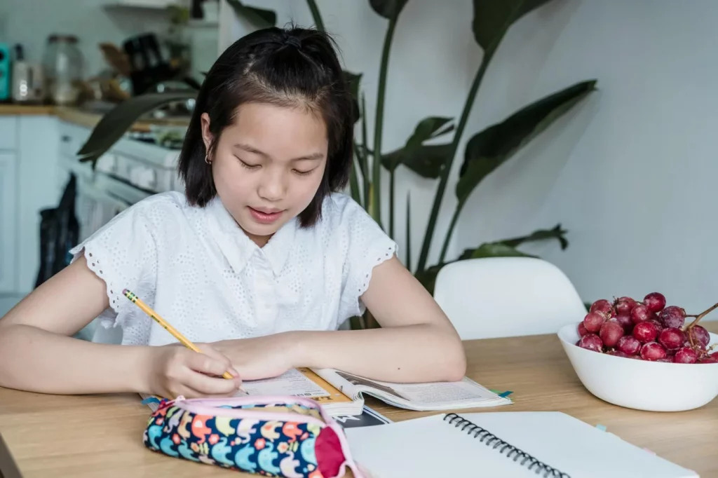 Asian teenage girl writing notes at home, representing brain food for studying and memory support