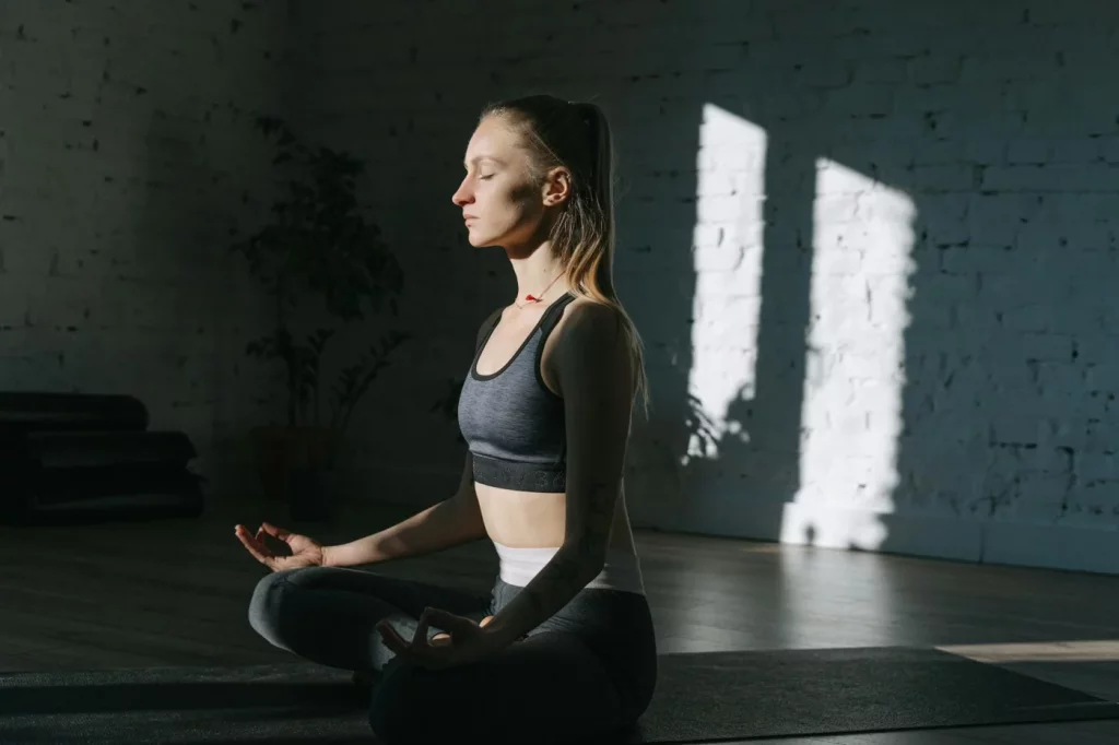 Woman meditating indoors in lotus position, practicing breathing exercises for stress and mindfulness