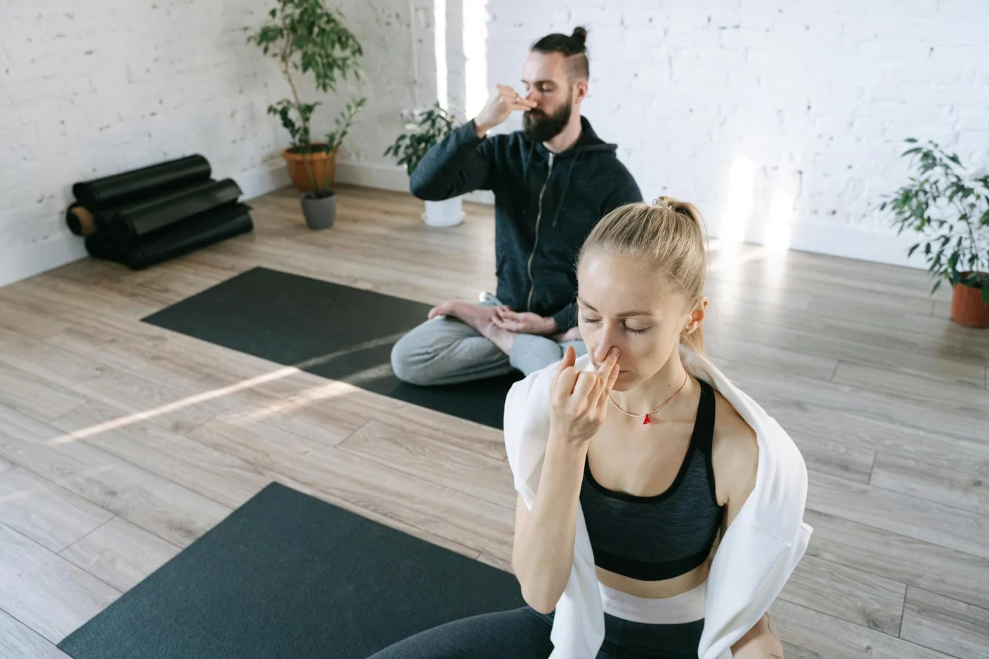 Two people practicing yoga breathing exercises for stress indoors, demonstrating a calming relaxation technique