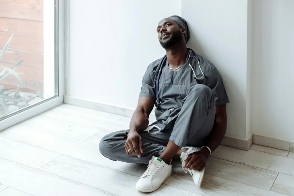 Healthcare worker in gray scrubs resting against a wall, illustrating burnout statistics by profession
