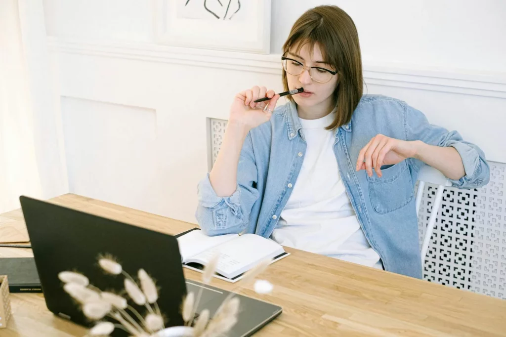 Woman in home office using cal newport deep work method with laptop and notebook, reflecting on focused work