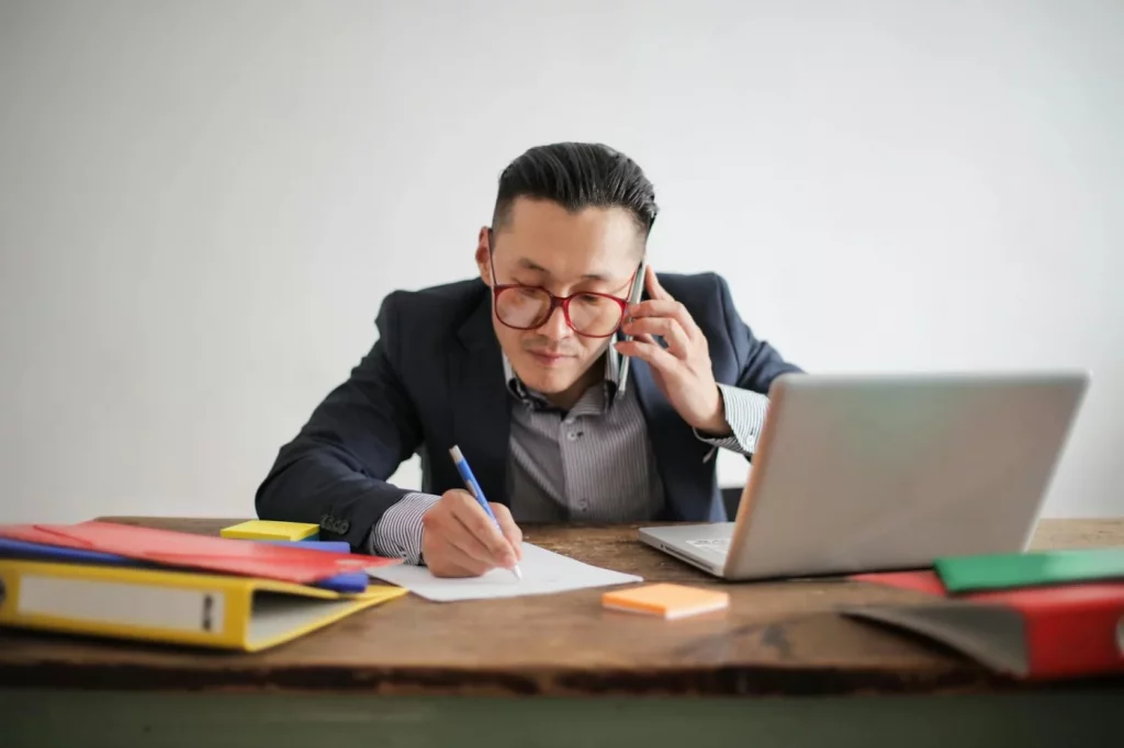 Businessman juggling a phone call, laptop, and notes at his desk, asking can your brain actually multitask