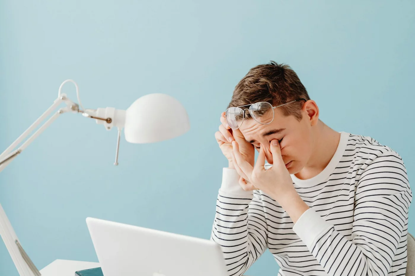 Do Blue Light Glasses Help With Eye Strain? Tired man rubbing eyes at laptop under desk lamp—do blue light glasses help with eye strain and screen fatigue symptoms?