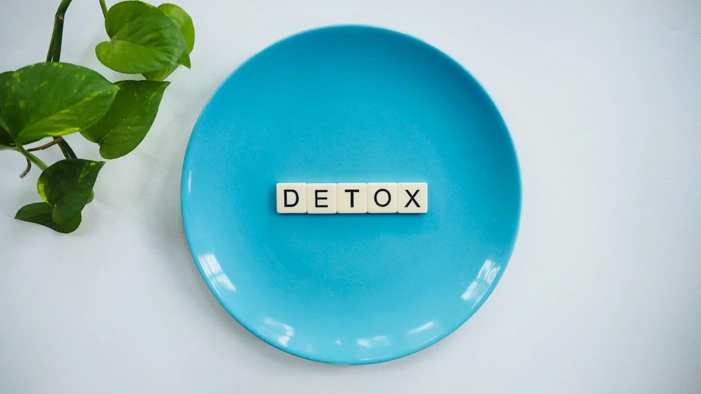 Detox letter tiles on a turquoise plate with green leaves, asking does dopamine detox work for adhd