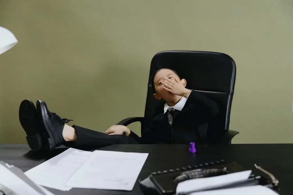 Why You Cannot Focus After Lunch: Causes and Fixes Child in a suit yawning at an office desk, illustrating why feeling sleepy after eating is called post-lunch fatigue