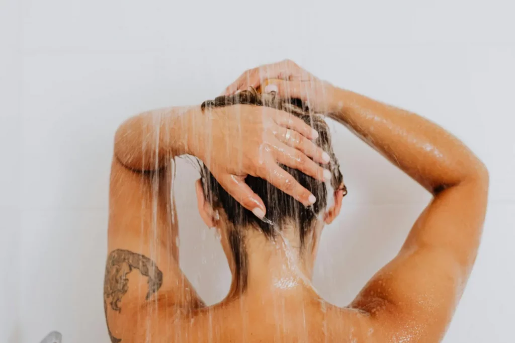 Cold Showers for Alertness and Focus: What Research Says Person showering with arm tattoo and running water, illustrating how long should a cold shower be