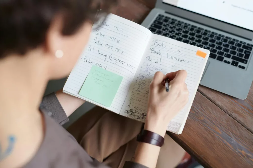 Adult writing in a notebook beside a laptop, illustrating how to build a second brain for organized work