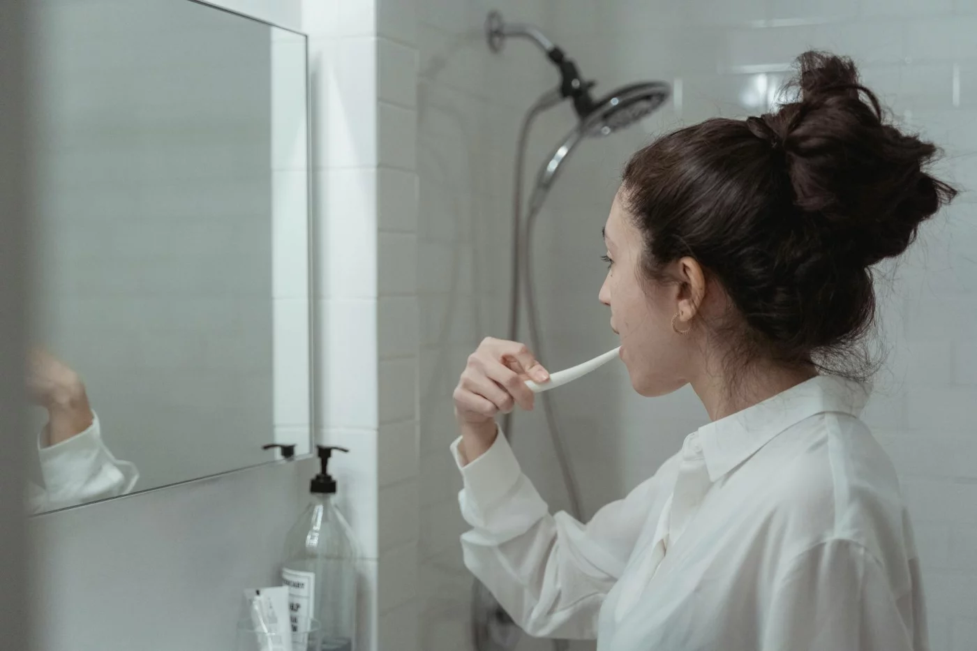 How to Build Habits That Stick With 8 Proven, Realistic Steps Woman brushing her teeth in a modern bathroom, showing how to build new habits that stick through daily routines