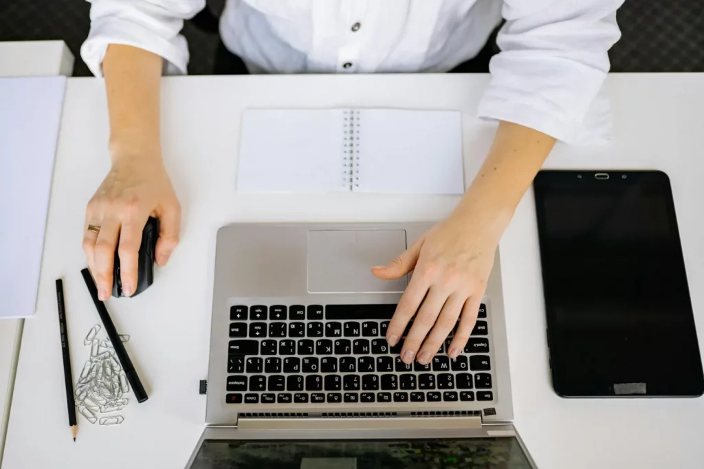 Top view of workspace with laptop and tablet, hands typing, showing how to set up a focused office desk