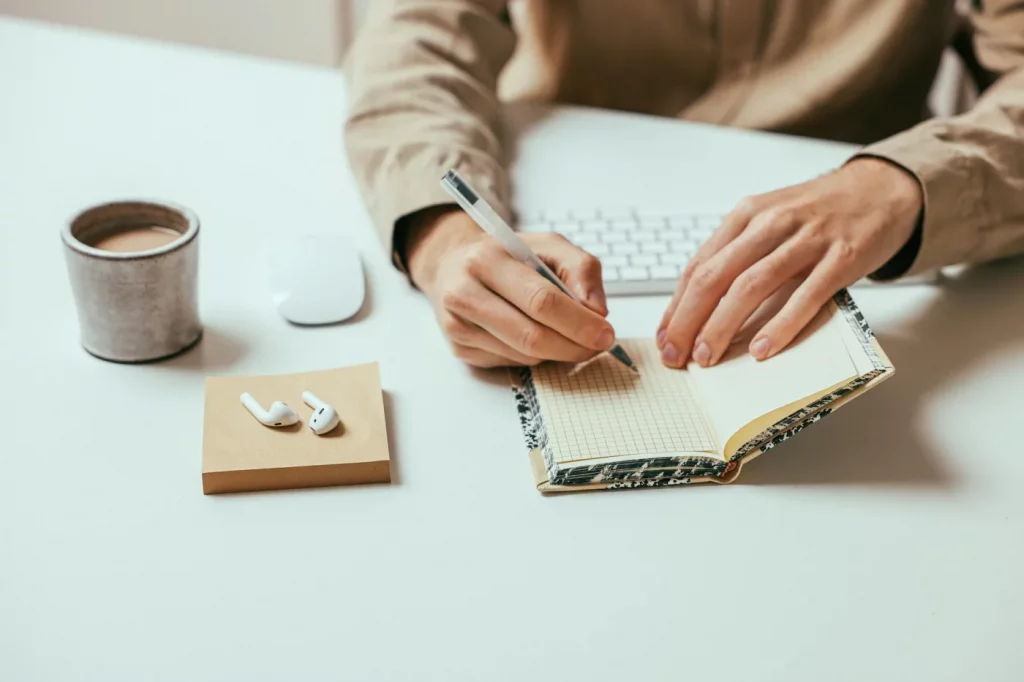 Person writing in a notebook at a desk with coffee and AirPods, how to focus with adhd without medication