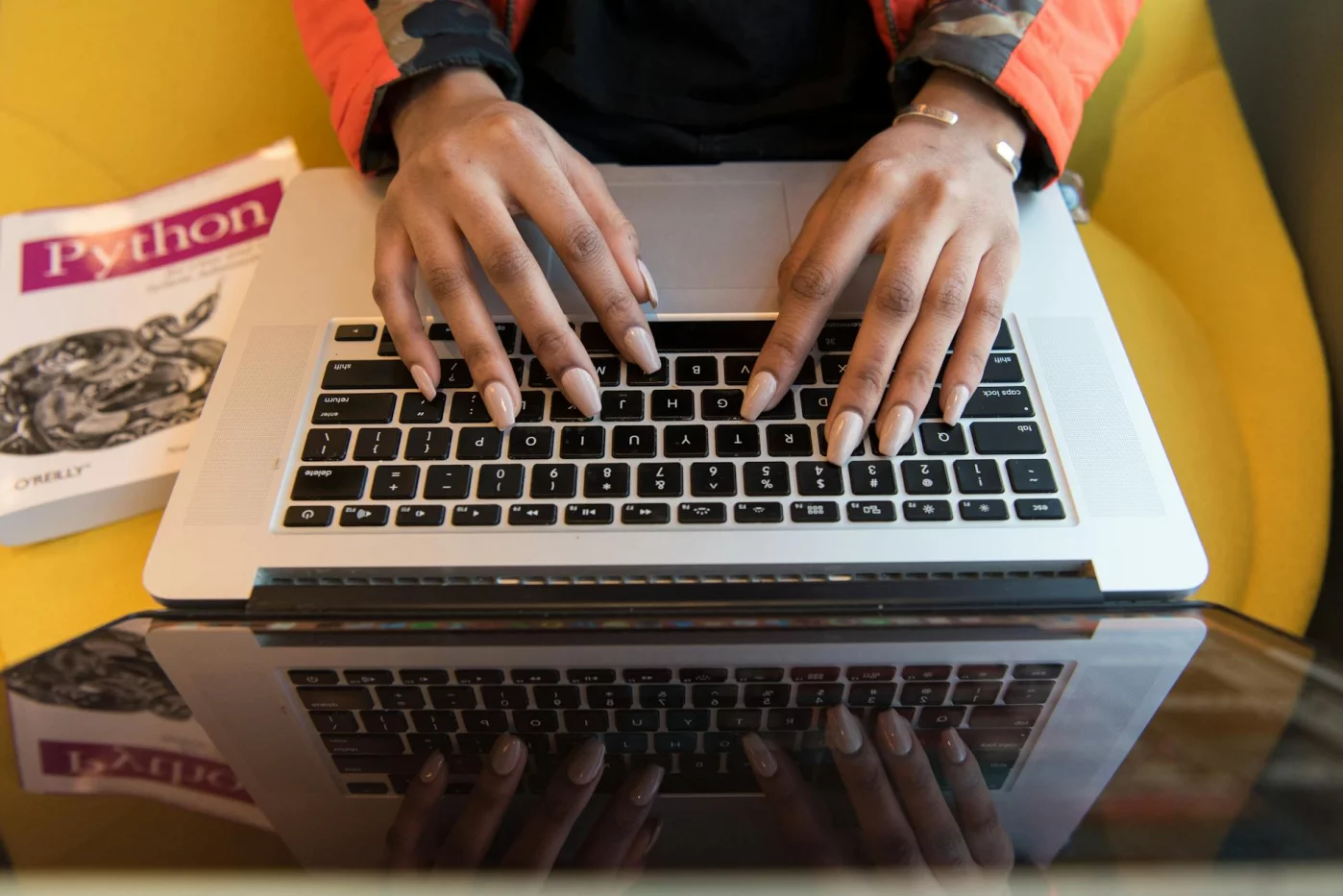 Person typing on a laptop beside a Python book, illustrating how to learn python faster with focused practice