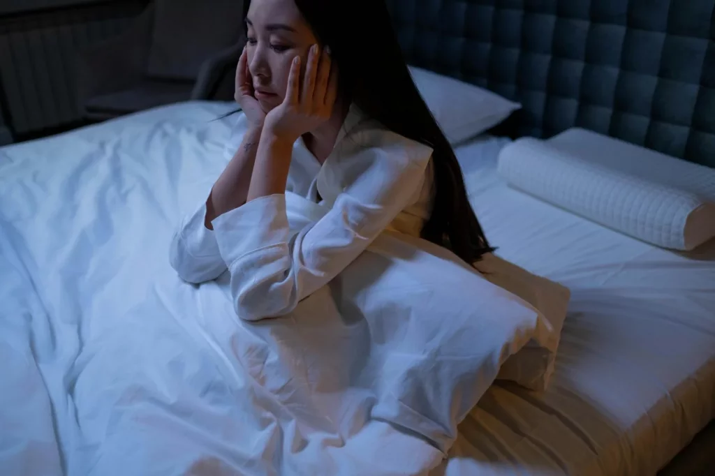 Asian woman awake in bed at night, illustrating how to sleep when stressed and anxious