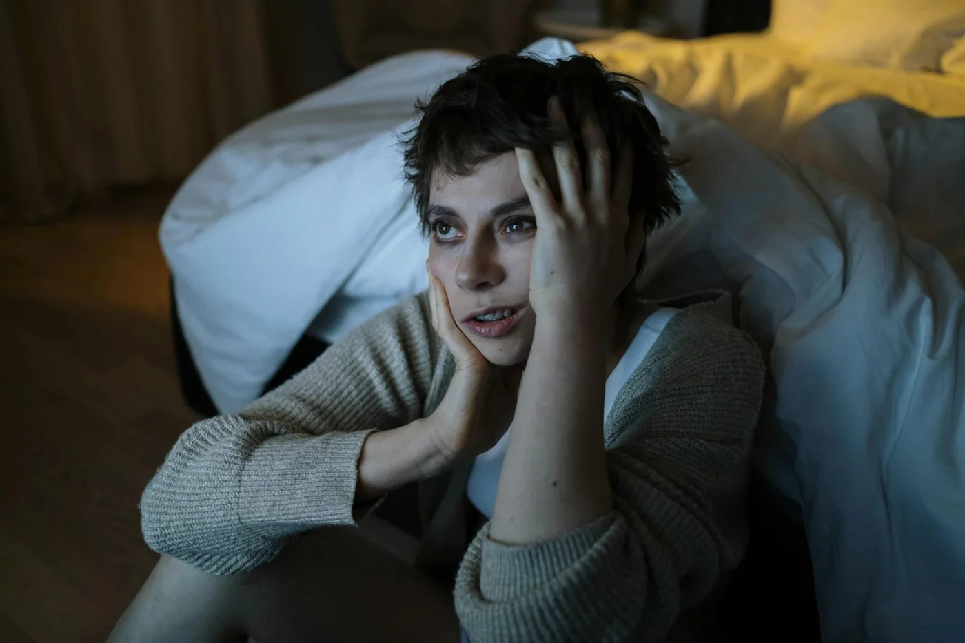 Woman by bed looking worried, illustrating how to sleep when stressed and anxious without forcing sleep