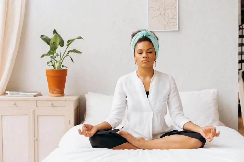 How to Build a Daily Meditation Practice That Actually Sticks Woman meditating on a bed indoors, showing how to start a daily meditation practice in a calm space
