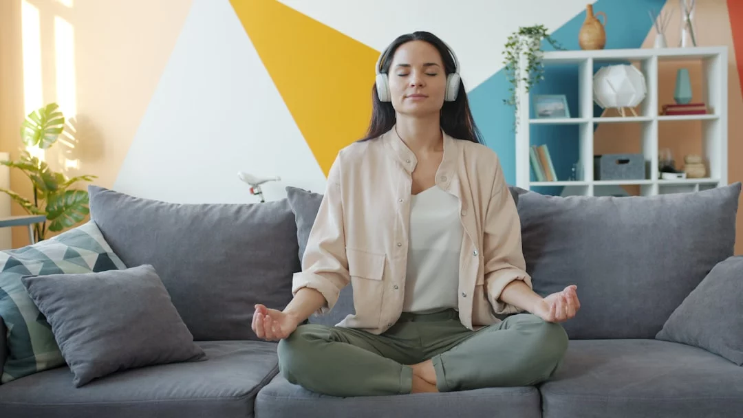 How to Build a Daily Meditation Practice That Actually Sticks Woman meditating on a couch with headphones, showing how to start a daily meditation practice at home