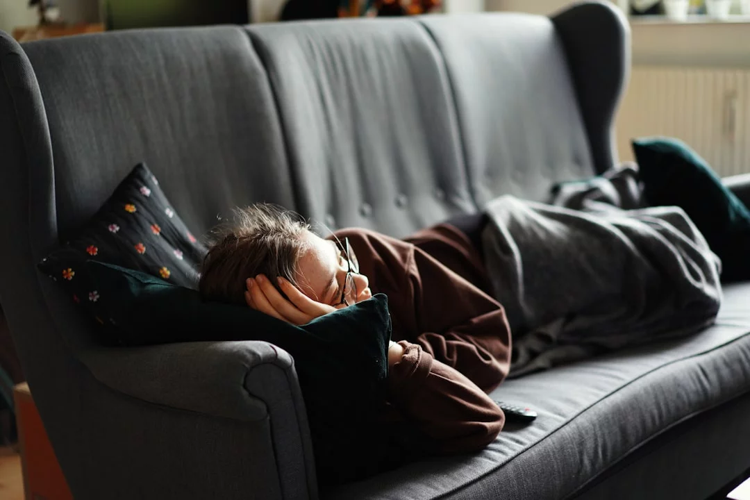 Woman in pink jacket on gray couch showing how to take power nap without oversleeping using nap time rules