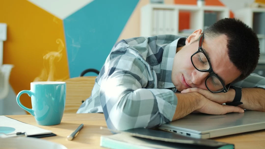 Man sleeping at desk with coffee nearby, showing how to take power nap without oversleeping for better focus