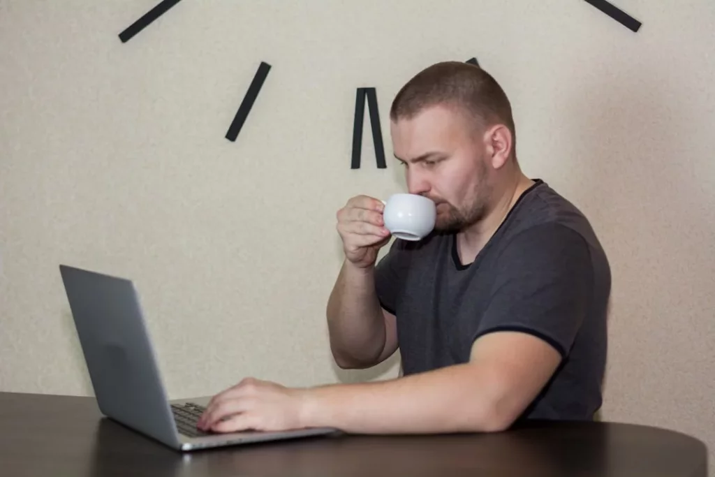 Man drinking coffee while using a laptop, exploring is chronotype real and peak performance habits
