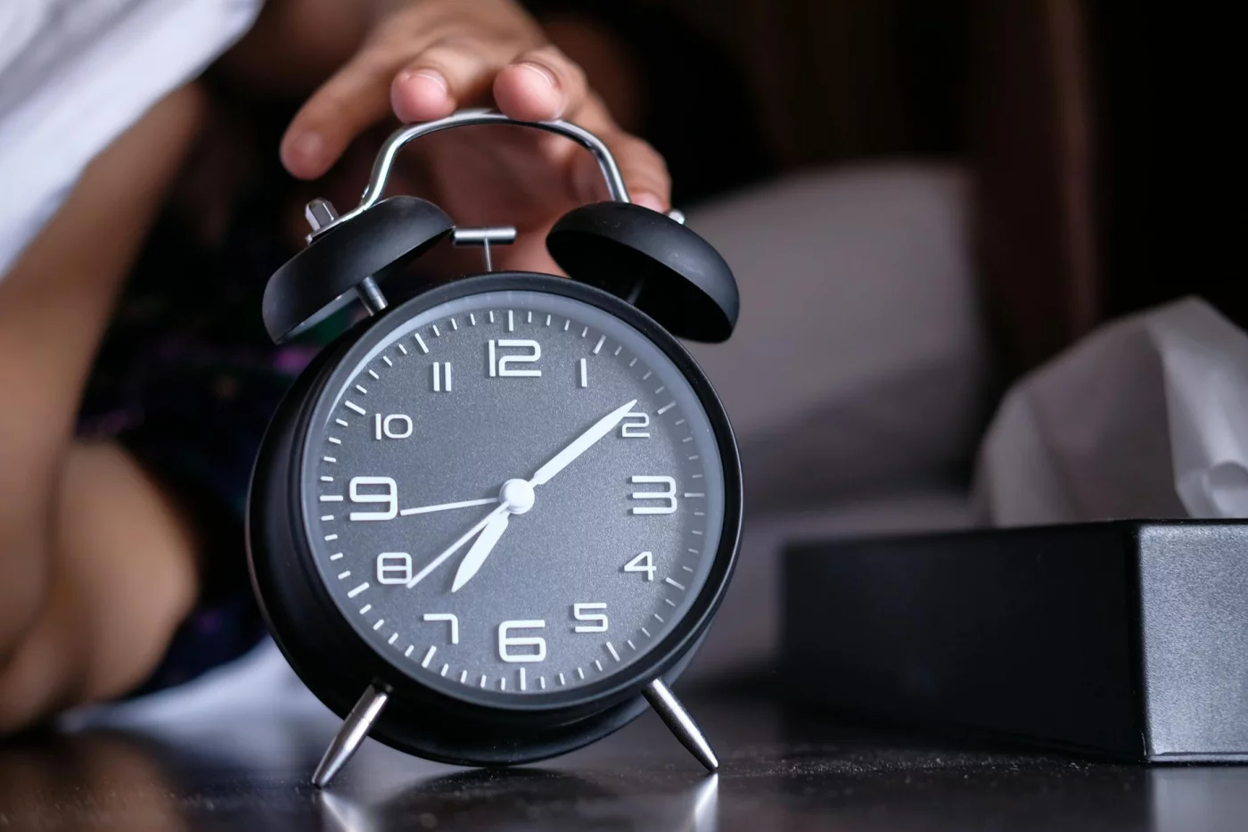 No-Phone Morning Routine: 9 Proven Benefits + Distraction-Free Templates Hand turning off an analogue alarm clock at dawn, showing no phone morning routine benefits for focus and clarity