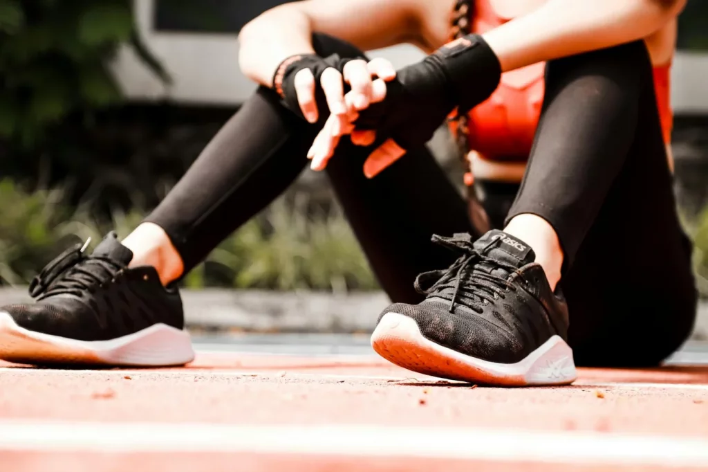 Female athlete resting on an outdoor track, wearing black sneakers and activewear, practicing personal energy management