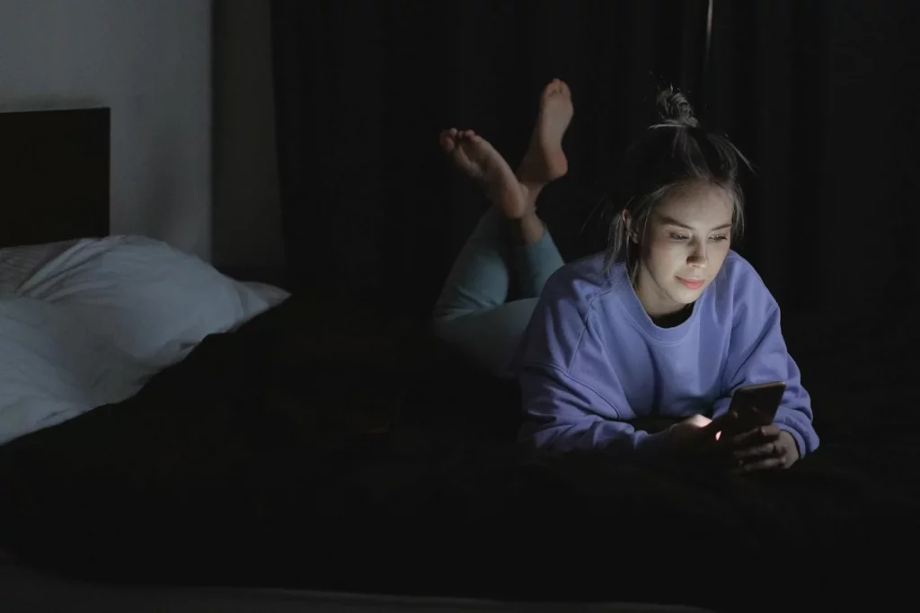 Woman in bed at night using smartphone, illustrating revenge bedtime procrastination and delayed sleep habits