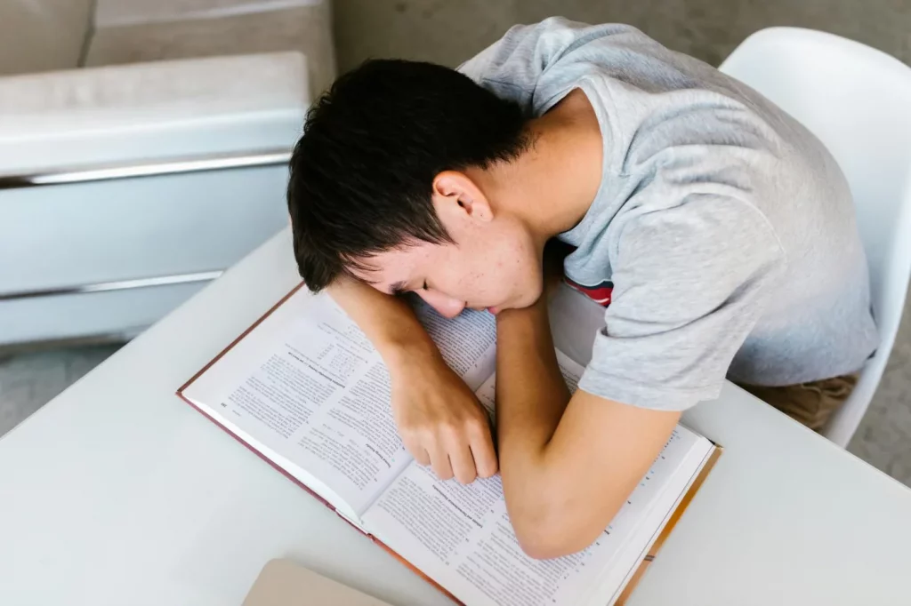 Student asleep at a desk with open textbook, illustrating sleep and memory consolidation during study fatigue