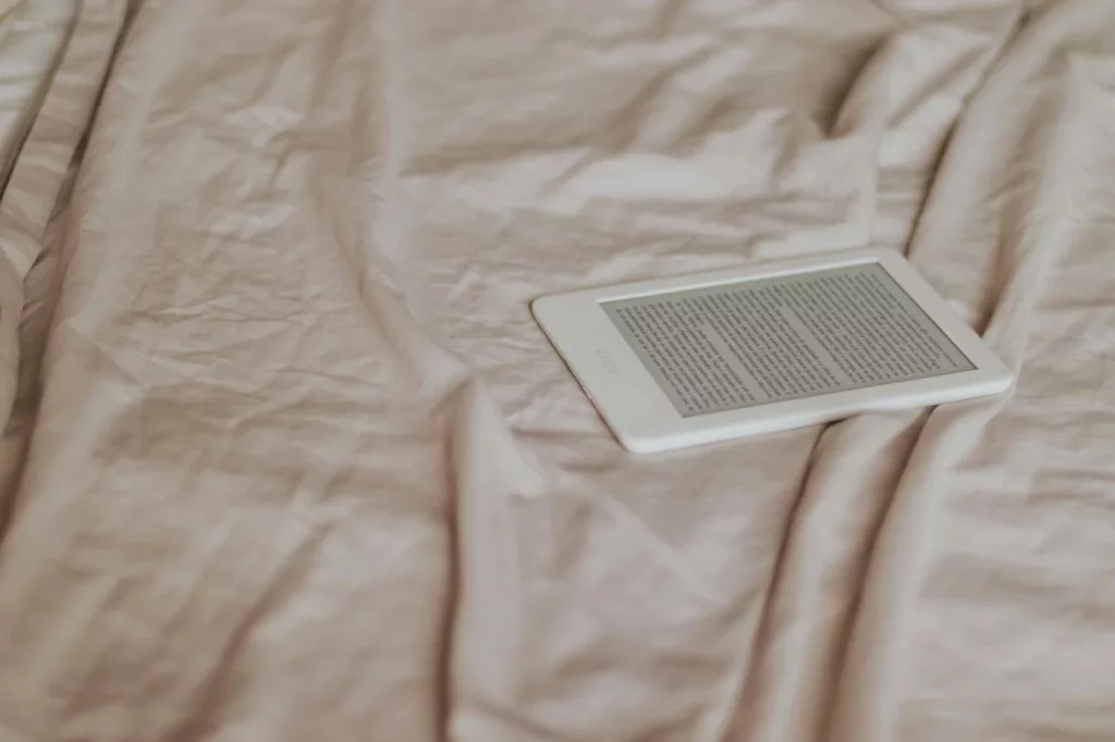 Minimalist e-reader on a beige crumpled bedspread displaying a sleep restriction therapy pdf in a cozy setting
