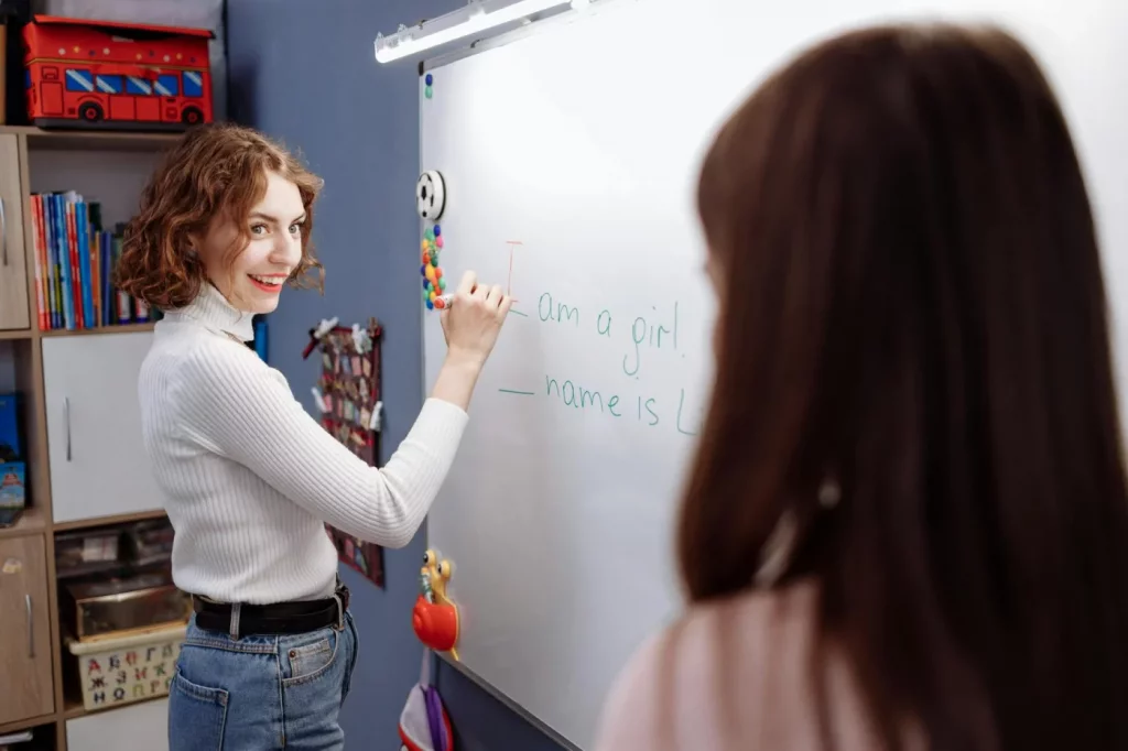 Smiling teacher at whiteboard explaining what is the Pareto Principle (80/20 rule) to students in a lively classroom