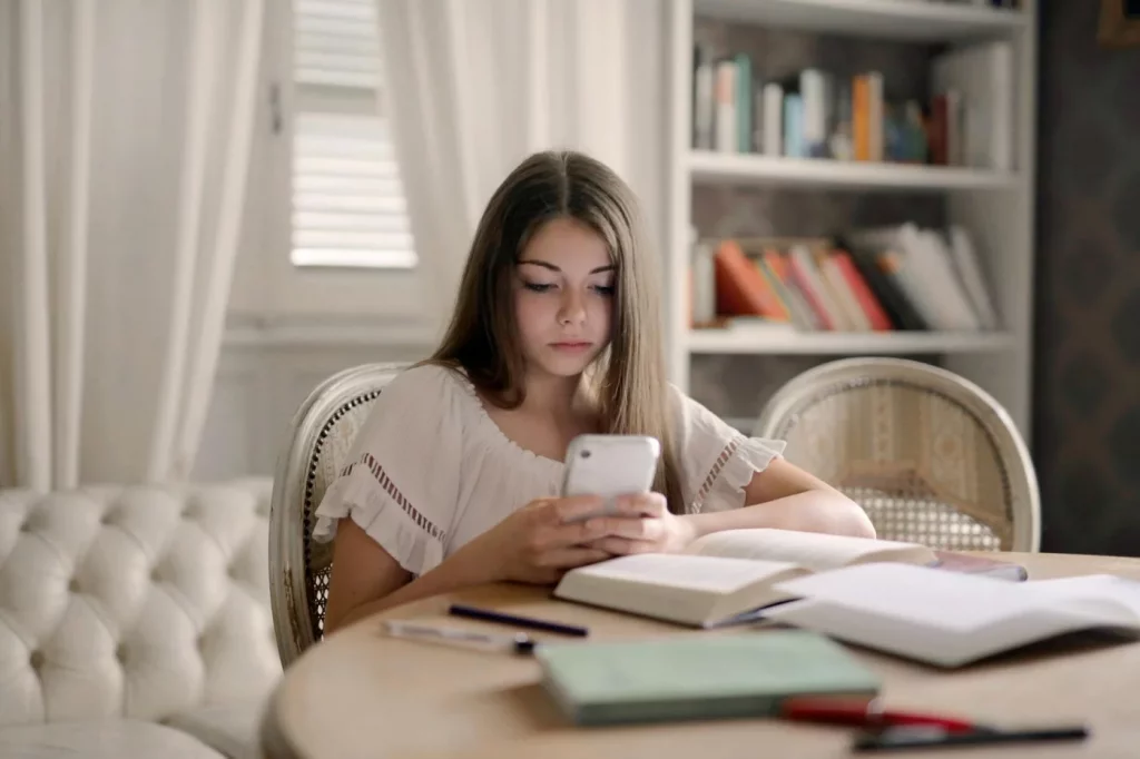 Teenage girl using ai homework help for students on her smartphone while studying at an indoor table