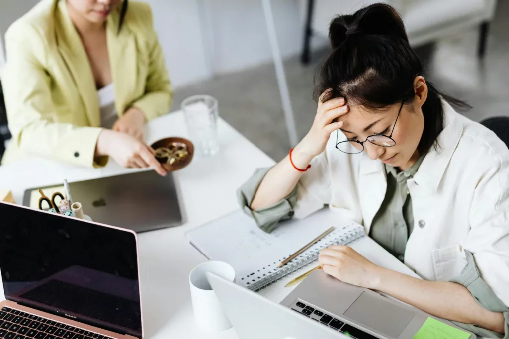 Woman in glasses stressed at her laptop, illustrating fear of failure procrastination at work