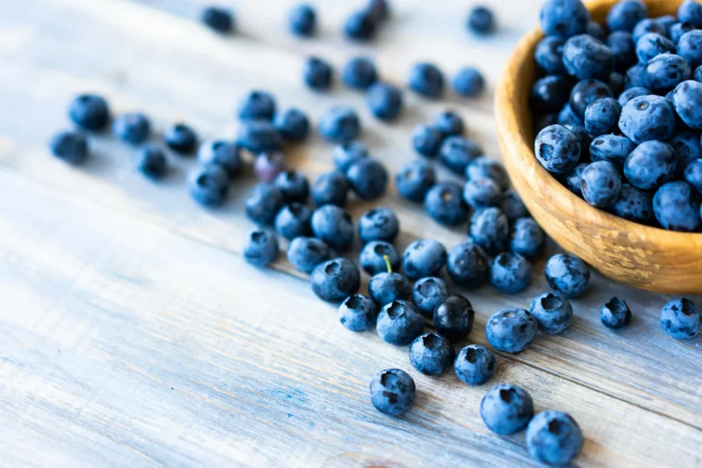 Fresh blueberries spilling from a wooden bowl, one of the foods that reduce oxidative stress