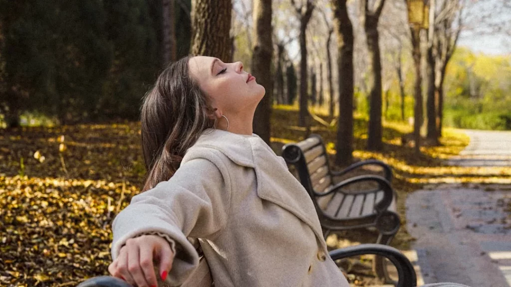 Woman relaxing on a park bench in autumn, reflecting on grounding techniques for overthinking