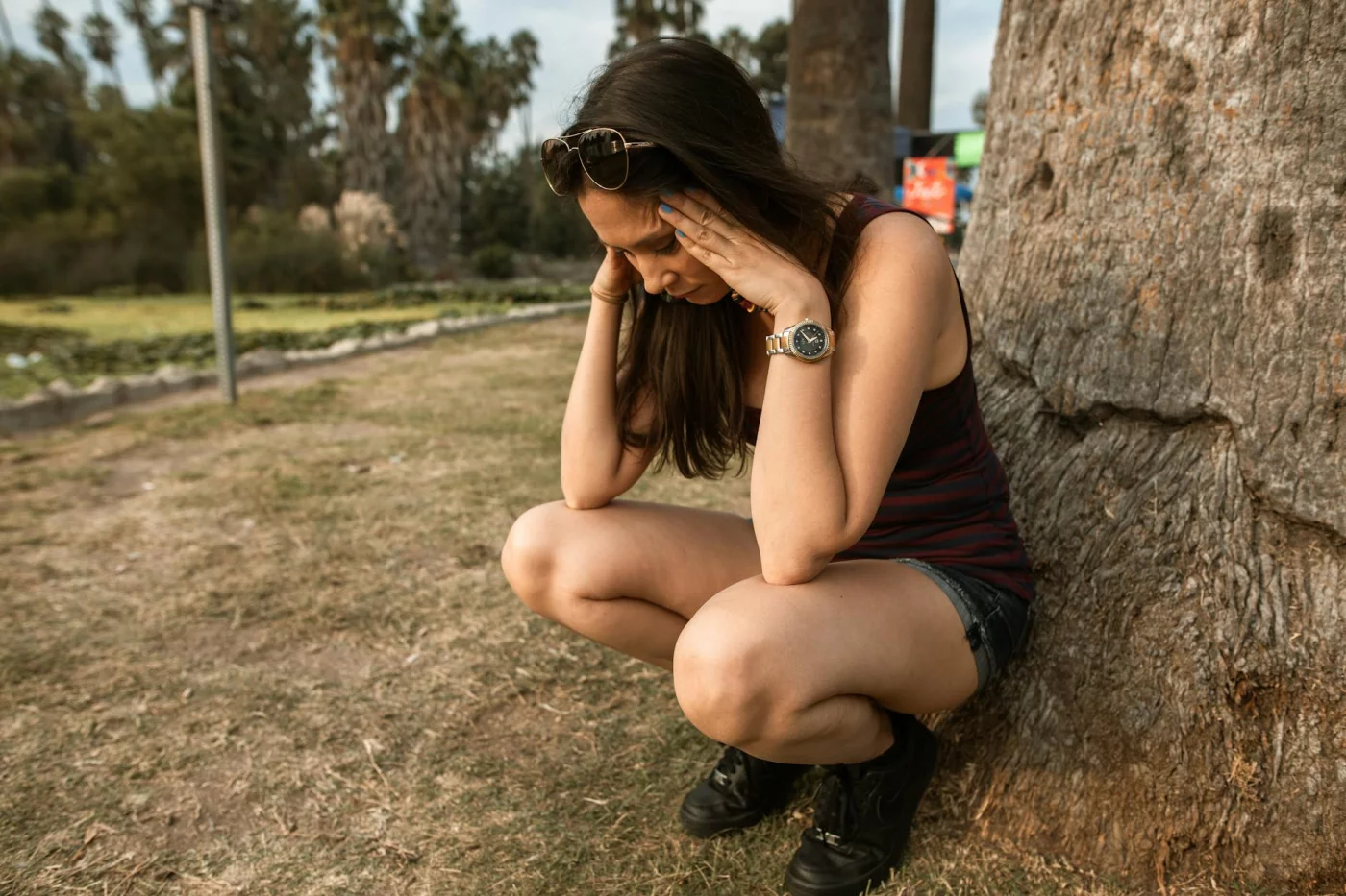 Grounding Techniques for Sudden Anxiety Spikes in Public Woman kneeling by a tree in a park using grounding techniques for overthinking during a stressful moment