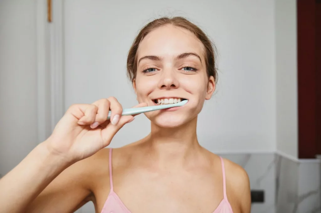 Habit Stacking: How to Pair New Habits With Old Ones Woman smiling while brushing her teeth in a modern bathroom, illustrating habit stacking examples