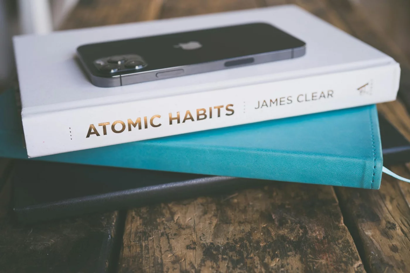 Habit Stacking: How to Pair New Habits With Old Ones Smartphone on a stack of books beside Atomic Habits, illustrating habit stacking examples and daily routines