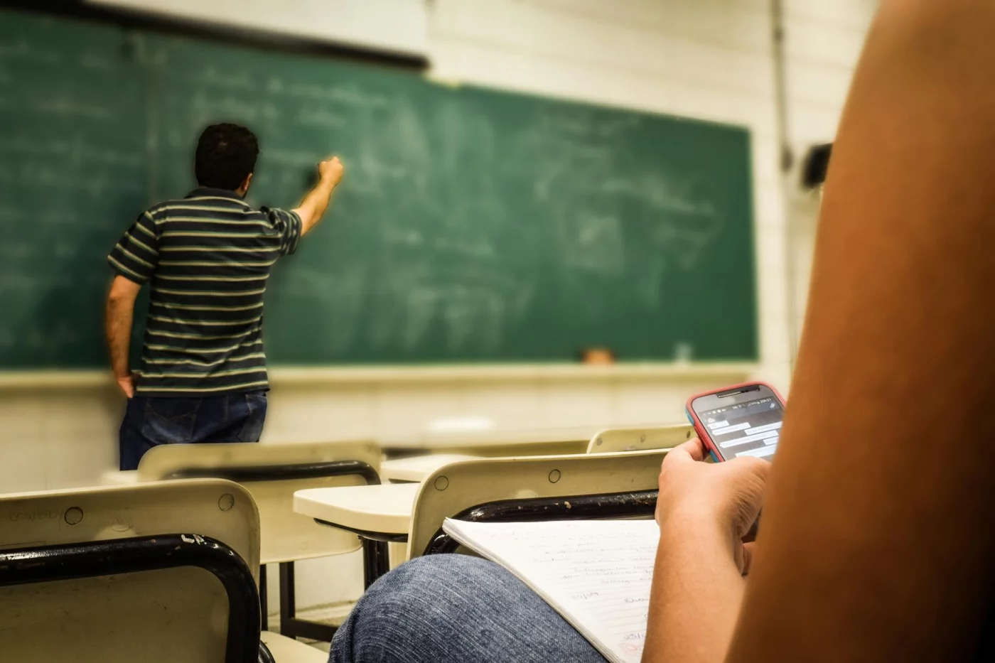 Student texting during class as the teacher writes on the board, showing how does attention affect learning