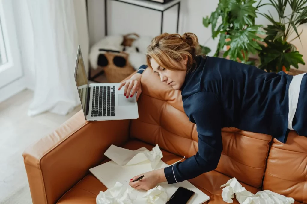 Woman resting on a couch with a laptop and papers, reflecting on how long does it take to decompress after work