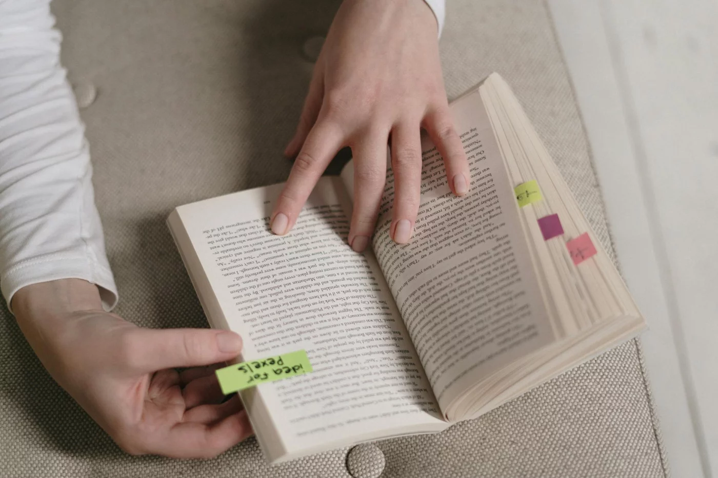 Hands holding an open book with colorful bookmarks, showing how to annotate a textbook in 7 smart steps