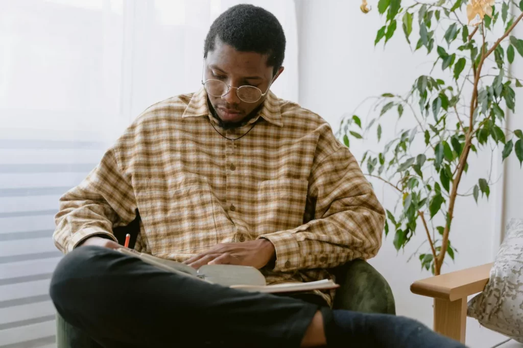 Man with glasses reading in a cozy, plant-filled room, illustrating how to read 50 books a year