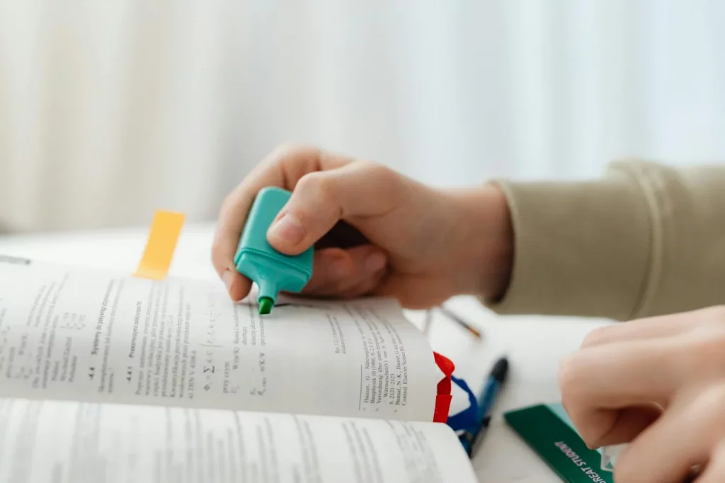 Student highlighting key passages in a textbook with a green marker while learning how to read dense textbooks