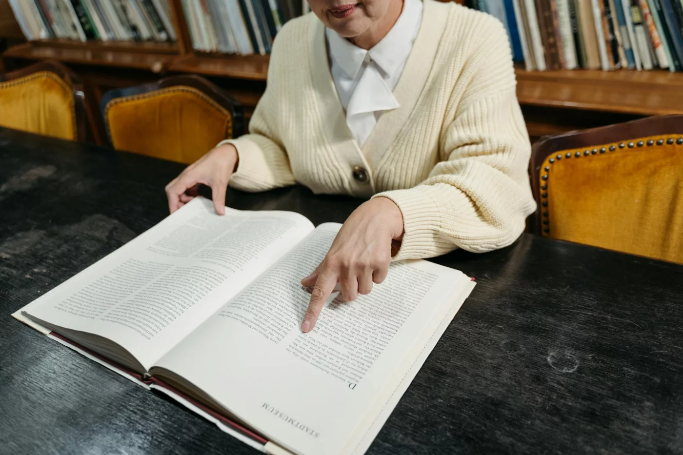 Student points to notes in an open book at a library table while learning how to read dense textbooks