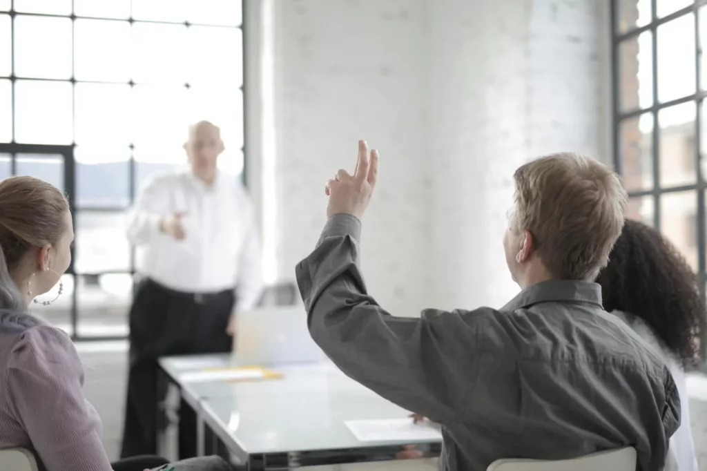 Employee raises hand in a team meeting while discussing how to set boundaries at work in a modern office