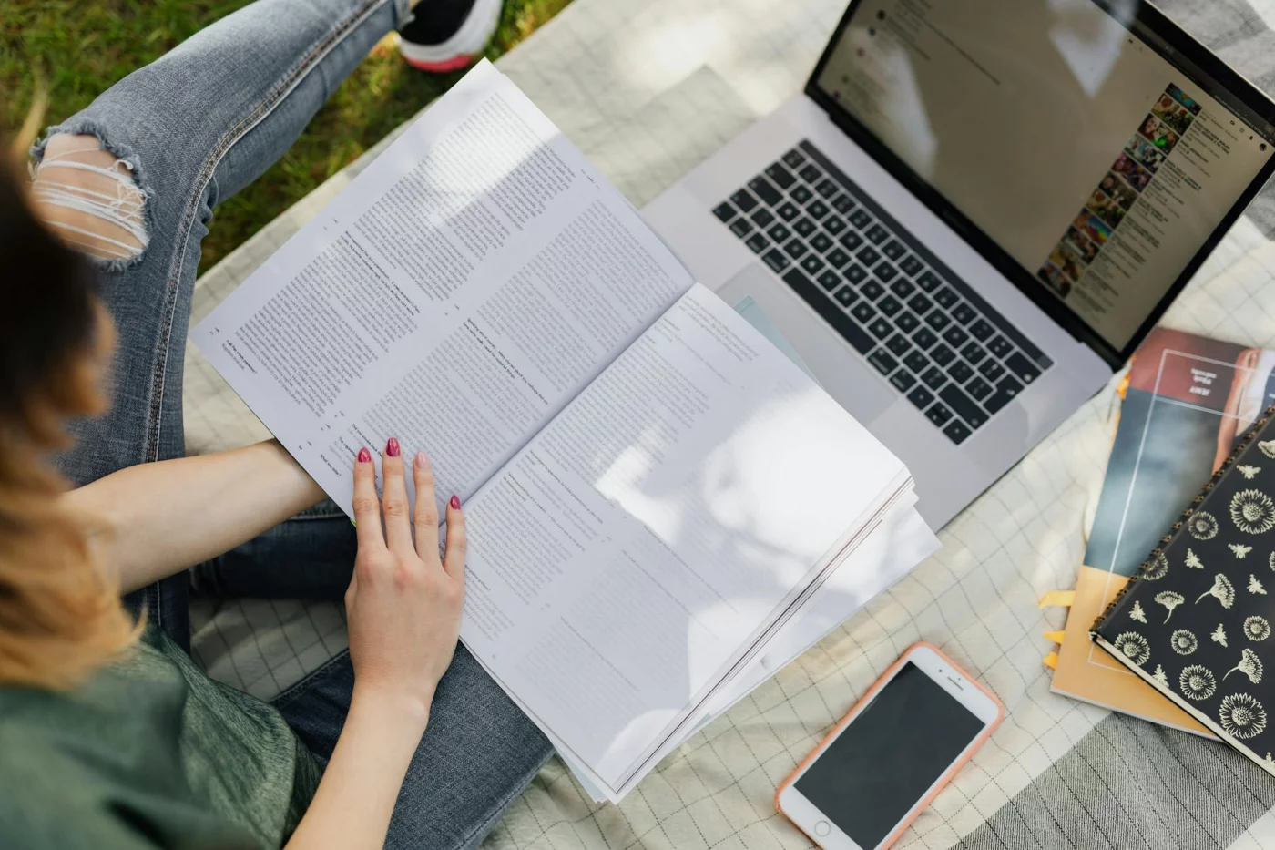 Student studying outdoors with a textbook, laptop, and phone while learning how to skim a textbook chapter