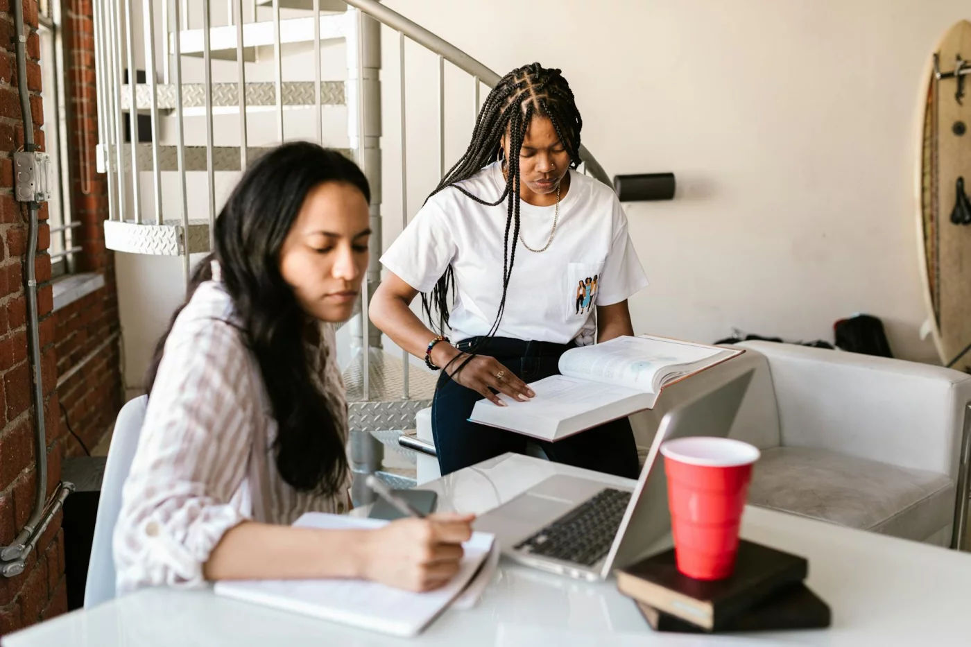 Interleaved Practice: How to Study Multiple Subjects in One Session College students studying together with a laptop and books, discussing interleaving practice indoors