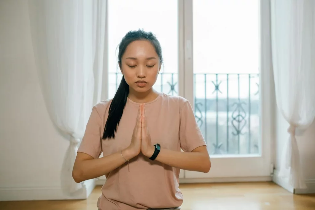 Mindfulness for People Who Can’t Sit Still Asian woman practicing mindfulness exercises for anxiety indoors with hands together in a calm meditation pose