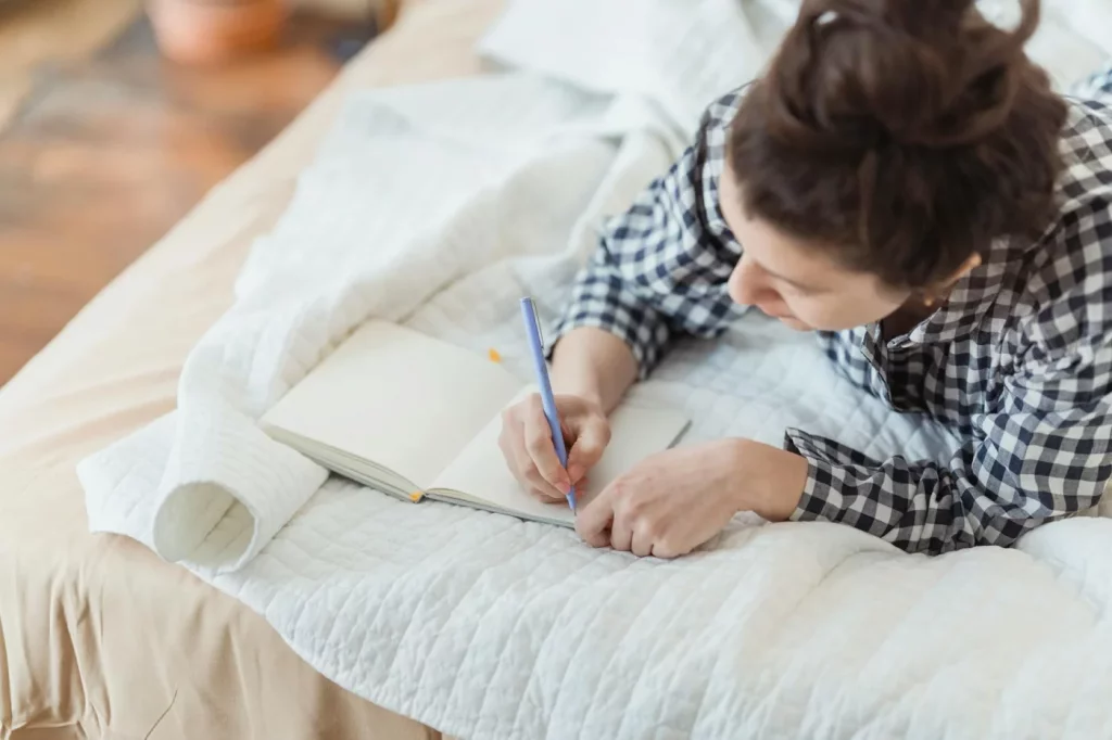 Woman journaling in bed as part of a scientifically proven best morning routine in a calm, softly lit bedroom
