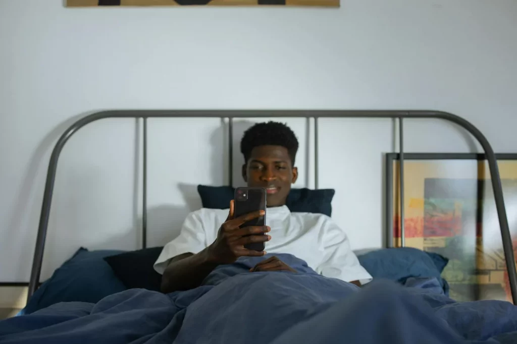 Young man using a smartphone in bed, illustrating the side effects of using phone at night