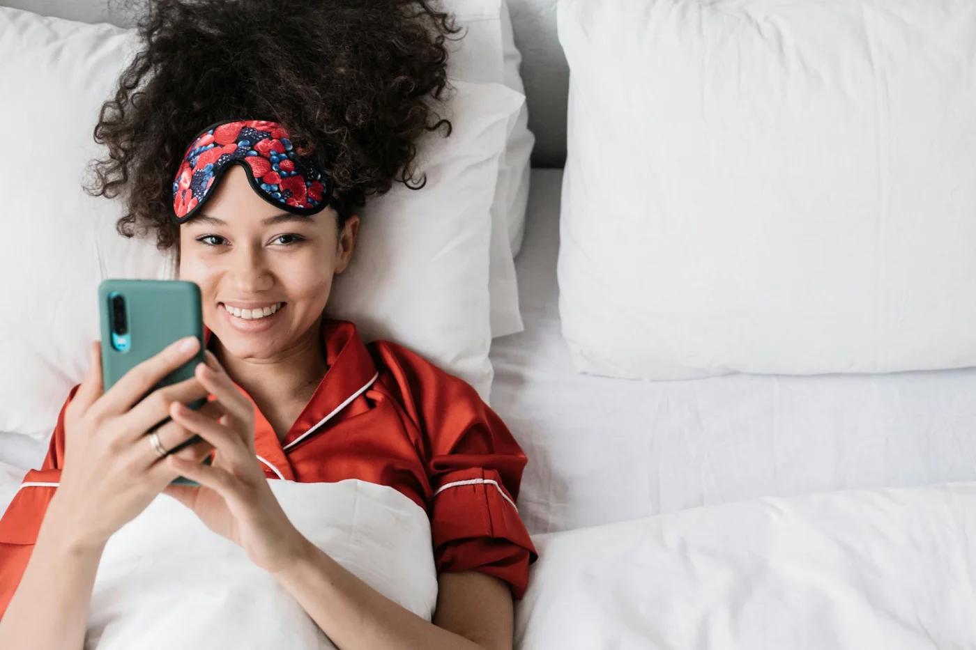 Woman in bed with a sleep mask using her phone at night, illustrating side effects of using phone at night