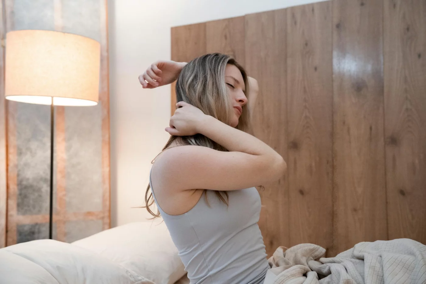 Woman stretching in bed in a bright bedroom, illustrating how sleep inertia can linger after waking